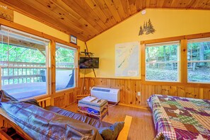 Uma cabana aconchegante com uma janela grande, uma TV de tela plana, um mapa na parede e um edredom acolchoado.
