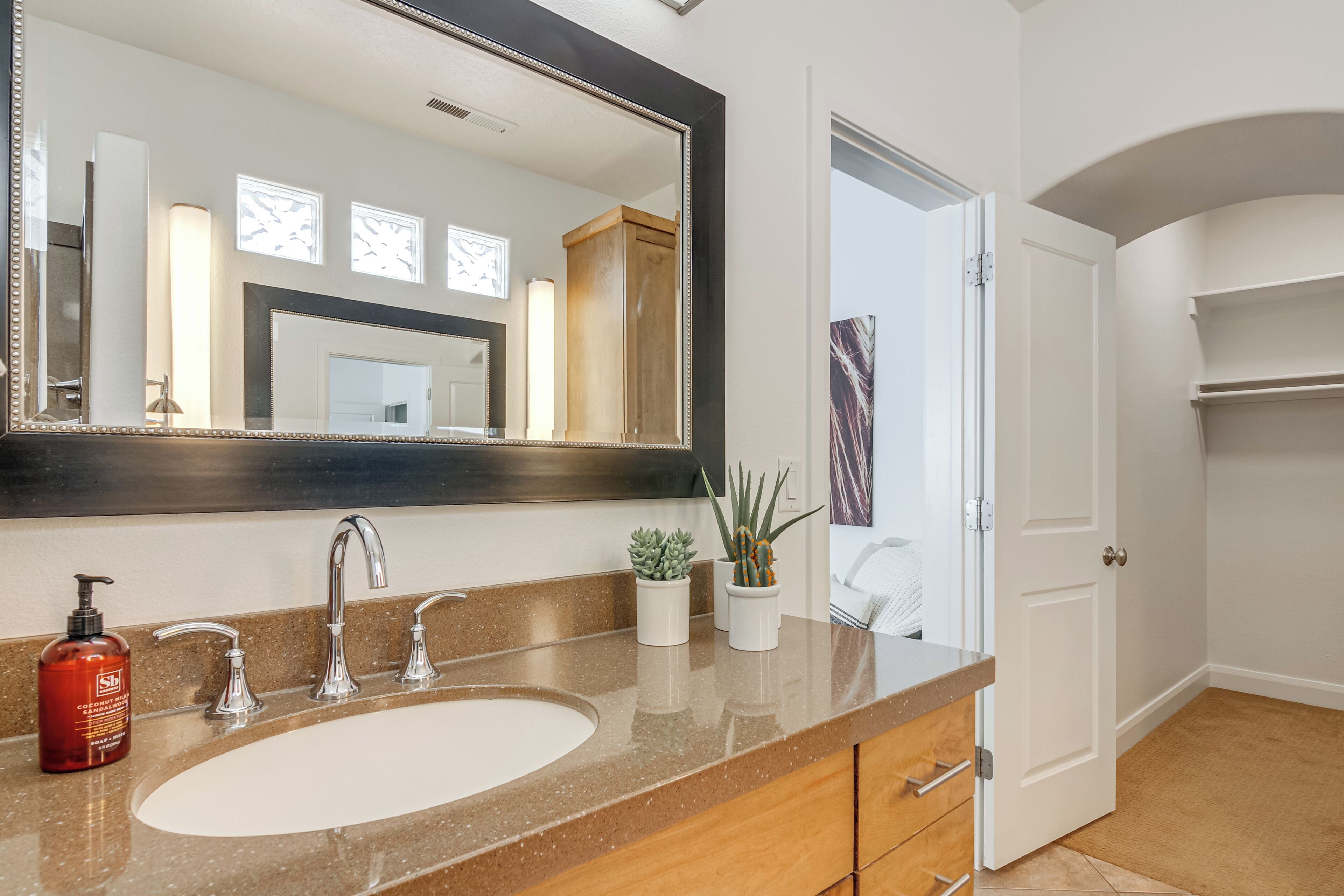 A bathroom with a large mirror, a sink, and two potted plants.