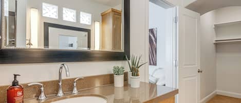 A bathroom with a large mirror, a sink, and two potted plants.
