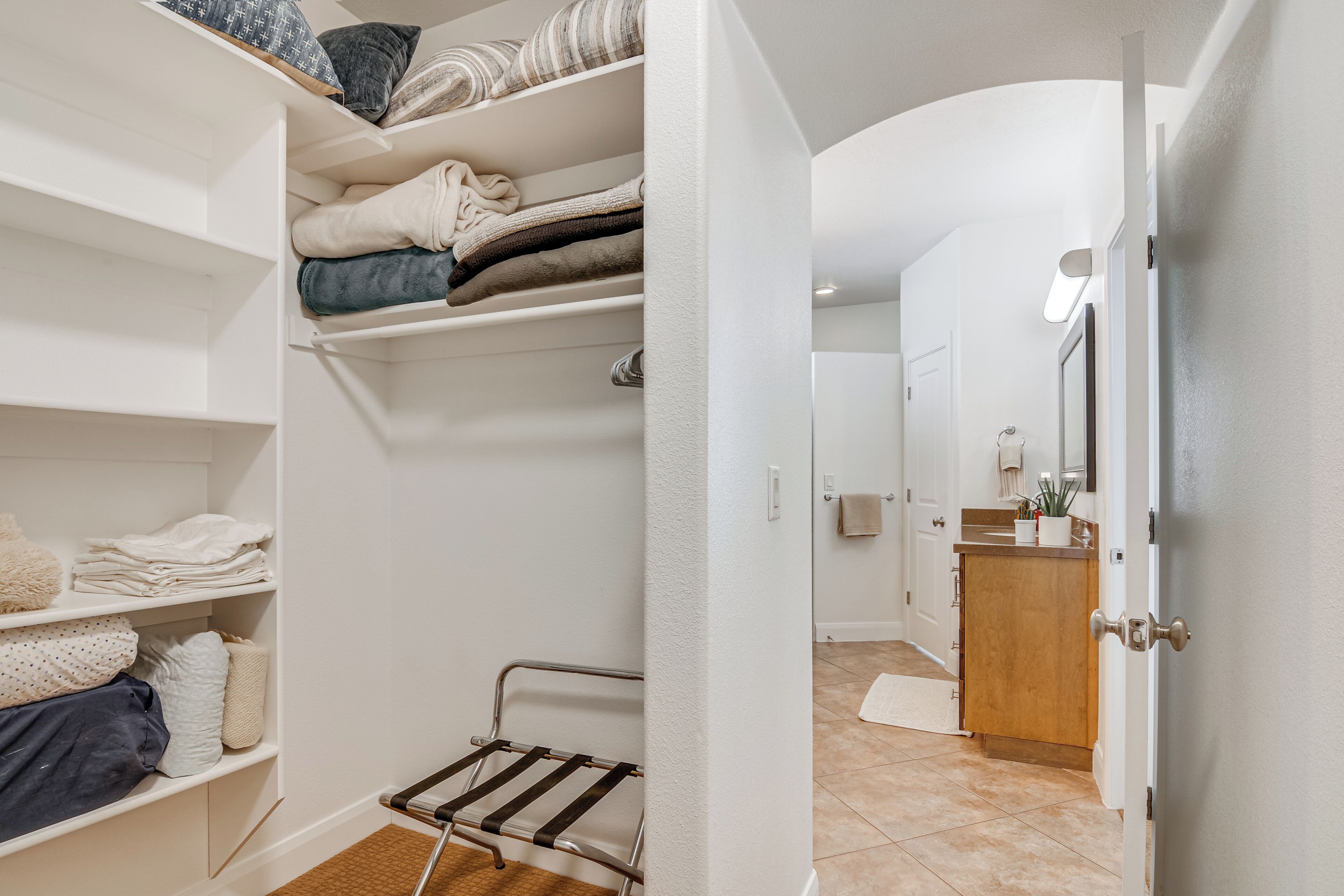 Un vestidor con repisas y un tendedero, un mueble de madera y una puerta que da a un baño.