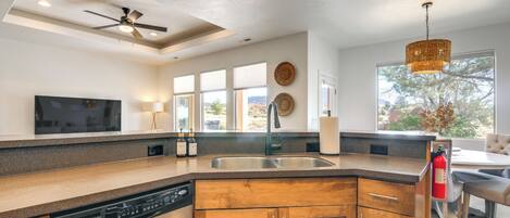 A modern kitchen with a dishwasher, wooden cabinets, a large island with a sink, a ceiling fan, and a dining area with a table and chairs.