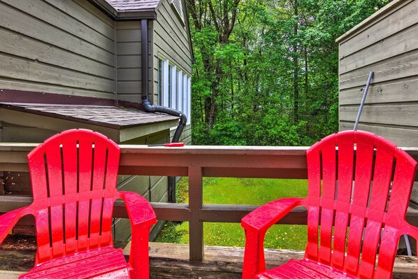 A wooden deck with two red Adirondack chairs and a table.