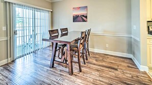 A dining area with a table and chairs, a large window with blinds, and a painting on the wall. - Steps to Pool: Myrtle Beach Vacation Rental! (Myrtle Beach)