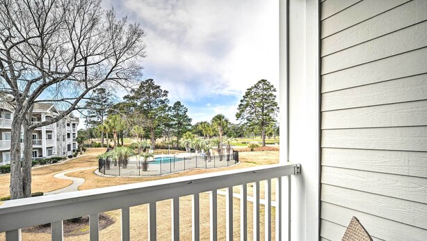 A view from a balcony overlooking a swimming pool, surrounded by trees and a building with a white exterior. - Steps to Pool: Myrtle Beach Vacation Rental! (Myrtle Beach)