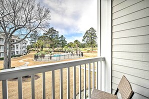 A view from a balcony overlooking a swimming pool, surrounded by trees and a building with a white exterior. - Steps to Pool: Myrtle Beach Vacation Rental! (Myrtle Beach)