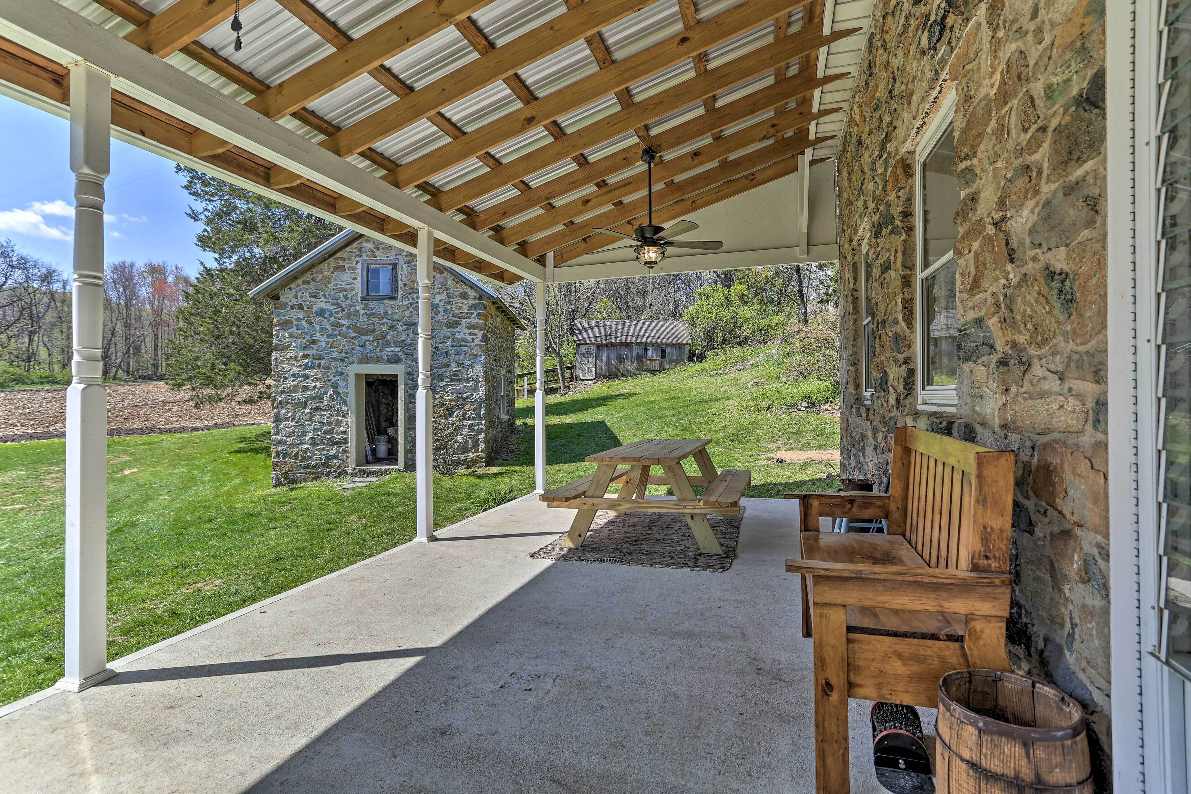 Un patio couvert avec un mur en pierre, un banc en bois, une table de pique-nique et un ventilateur de plafond.