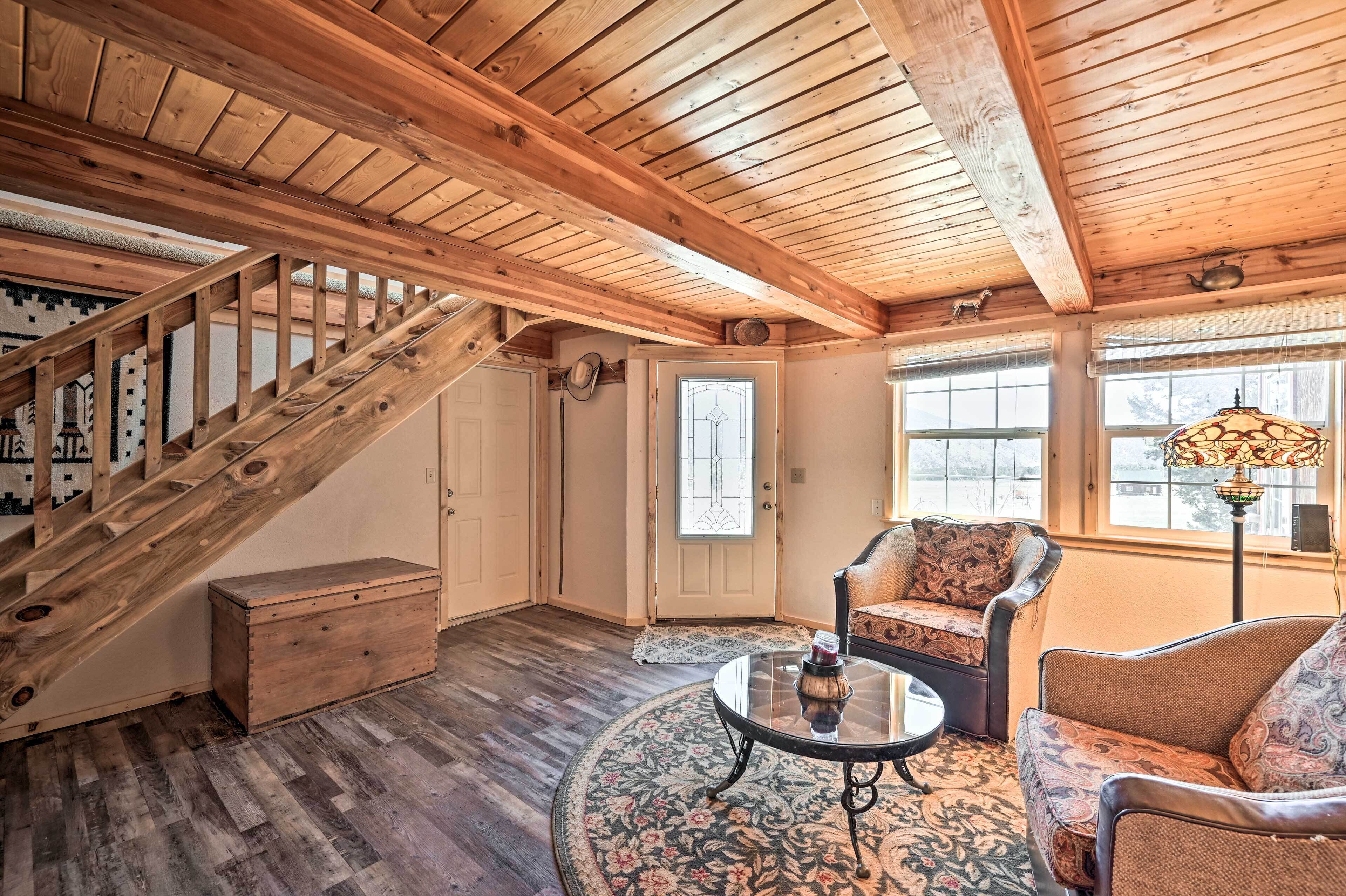A wooden interior with a staircase, a round table, and two patterned chairs.