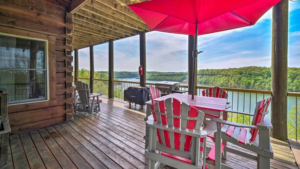 A wooden deck with a covered area, red Adirondack chairs, a table, and a red umbrella. - Spacious Cabin on Dale Hollow Lake w/ Hot Tub! (Albany)