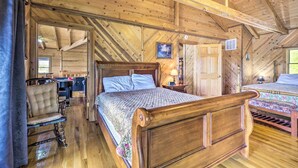 A wooden cabin bedroom with a large bed, a chair, a desk, and a window. - Spacious Cabin on Dale Hollow Lake w/ Hot Tub! (Albany)