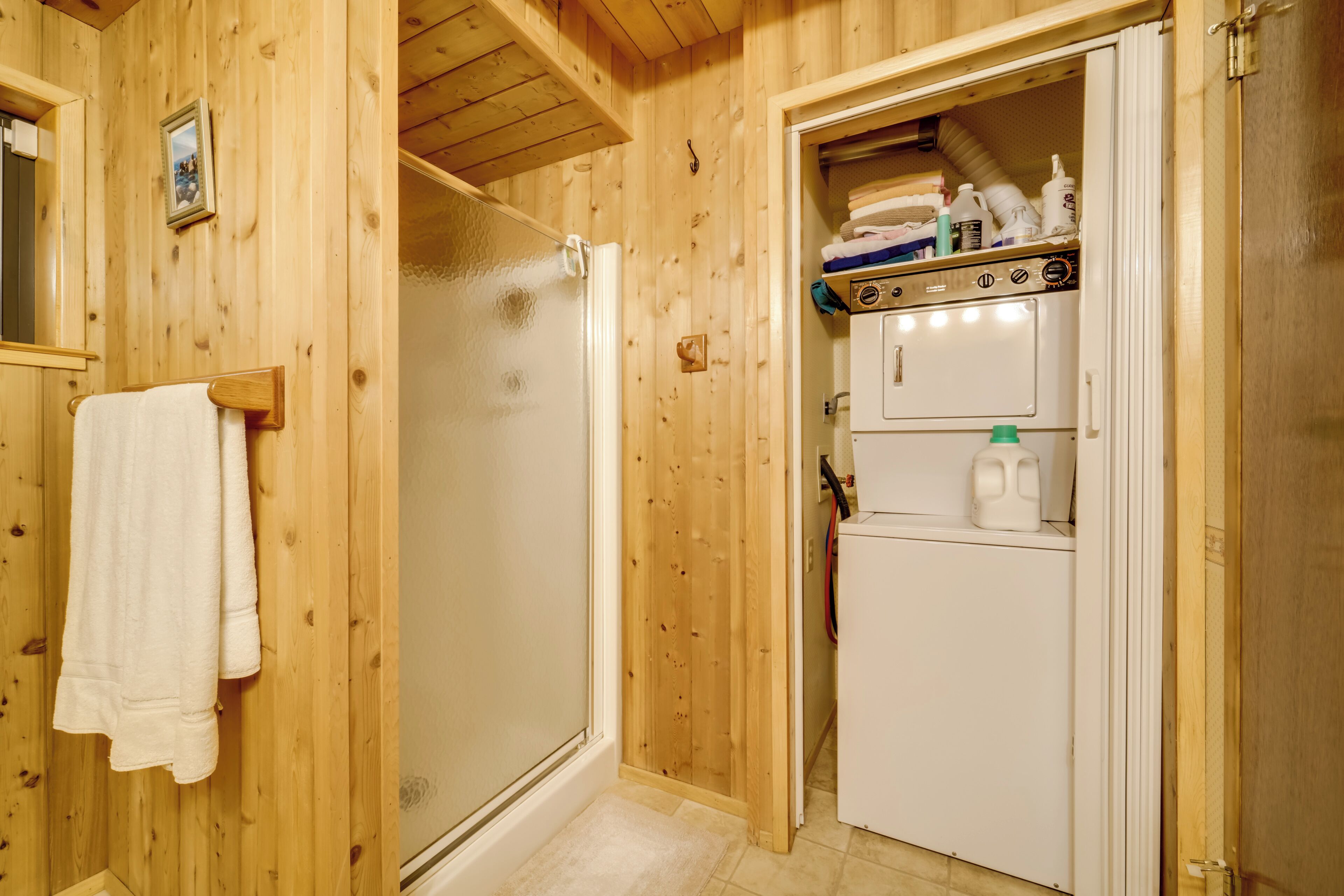 A wooden-paneled bathroom with a shower, a towel rack, and a small refrigerator with bottles on top.