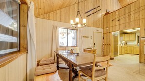 Ein Holzinterieur mit Esstisch, Stühlen, einer Chandelierleuchtre und Blick ins Freie.