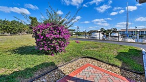 A grassy area with a paved walkway, a small brick section, and a bush with purple flowers. - Everglades Studio W/marina View, Patio+pool Access (Naples)