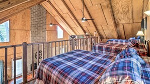 A loft-style bedroom with wooden beams, a brick fireplace, and plaid bedding. - Calico Rock Home, Walk to White River & Dtwn! (Calico Rock)