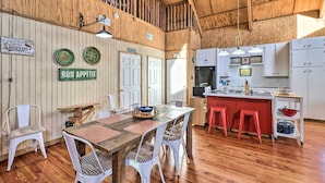A rustic kitchen with wooden walls, a wooden dining table with white chairs, a kitchen island with stools, and signs indicating guest areas. - Calico Rock Home, Walk to White River & Dtwn! (Calico Rock)