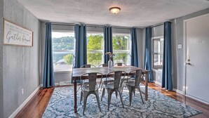 A dining area with a wooden table and chairs, blue curtains, and a view of greenery outside.