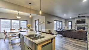 A spacious kitchen with a large island, wooden cabinets, and a stone fireplace. There are multiple windows providing natural light and views of the outdoors. - Lakefront Wisconsin Dells Home w/ Game Room (Wisconsin Dells)