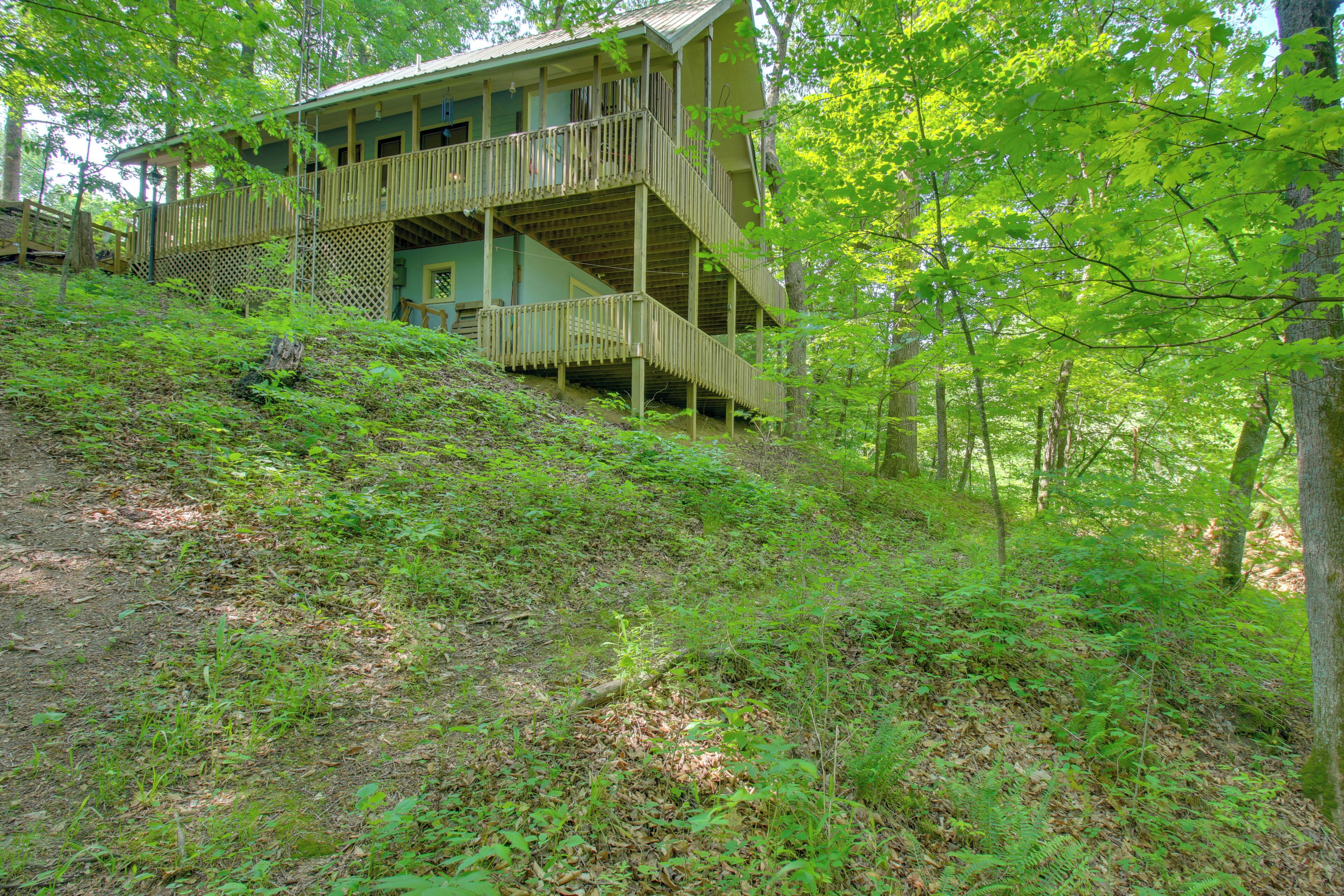 A multi-story wooden cabin with a balcony, surrounded by dense forest.