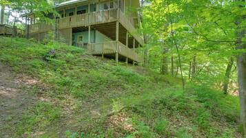 A multi-story wooden cabin with a balcony, surrounded by dense forest.