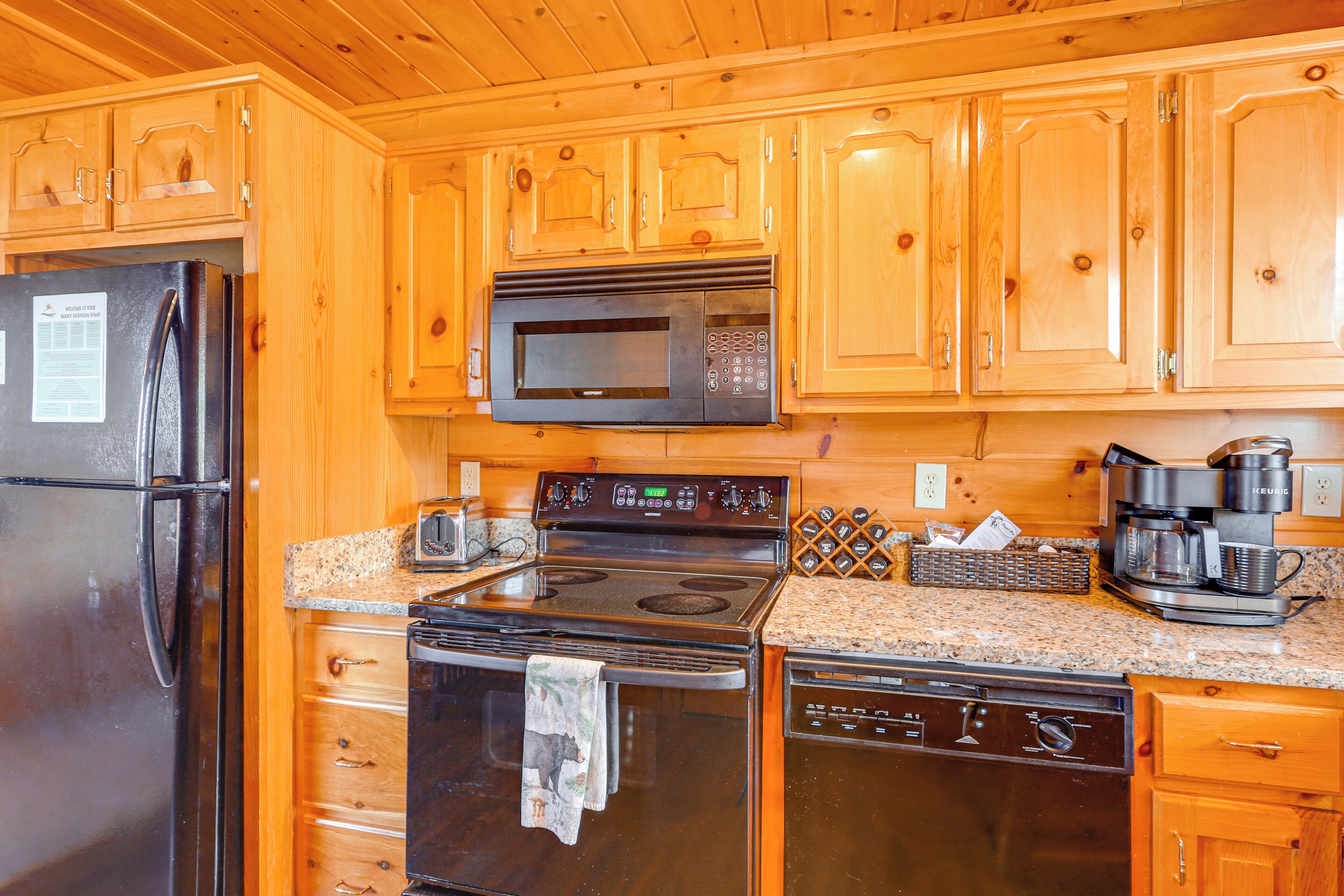 Una cocina con armarios de madera, un refrigerador de acero inoxidable, un microondas, una estufa, un lavavajillas y una cafetera.