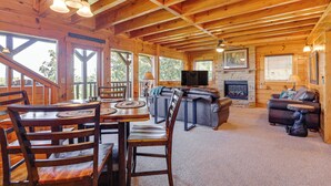 A wooden cabin interior with a dining area, sofas, and a fireplace.