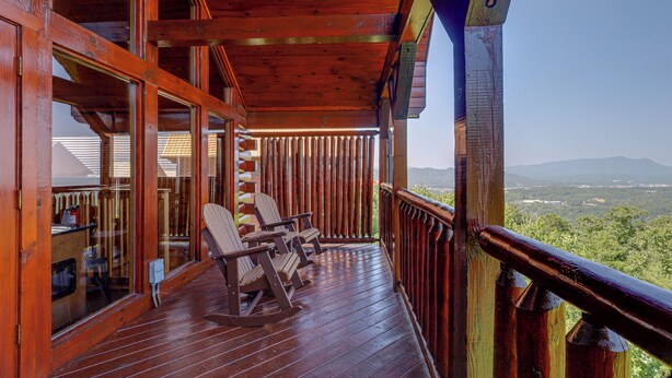 A wooden deck with rocking chairs and a view of a mountainous landscape.