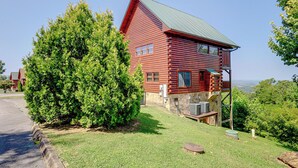 A red log cabin with a green roof, a stone foundation, and a small porch.