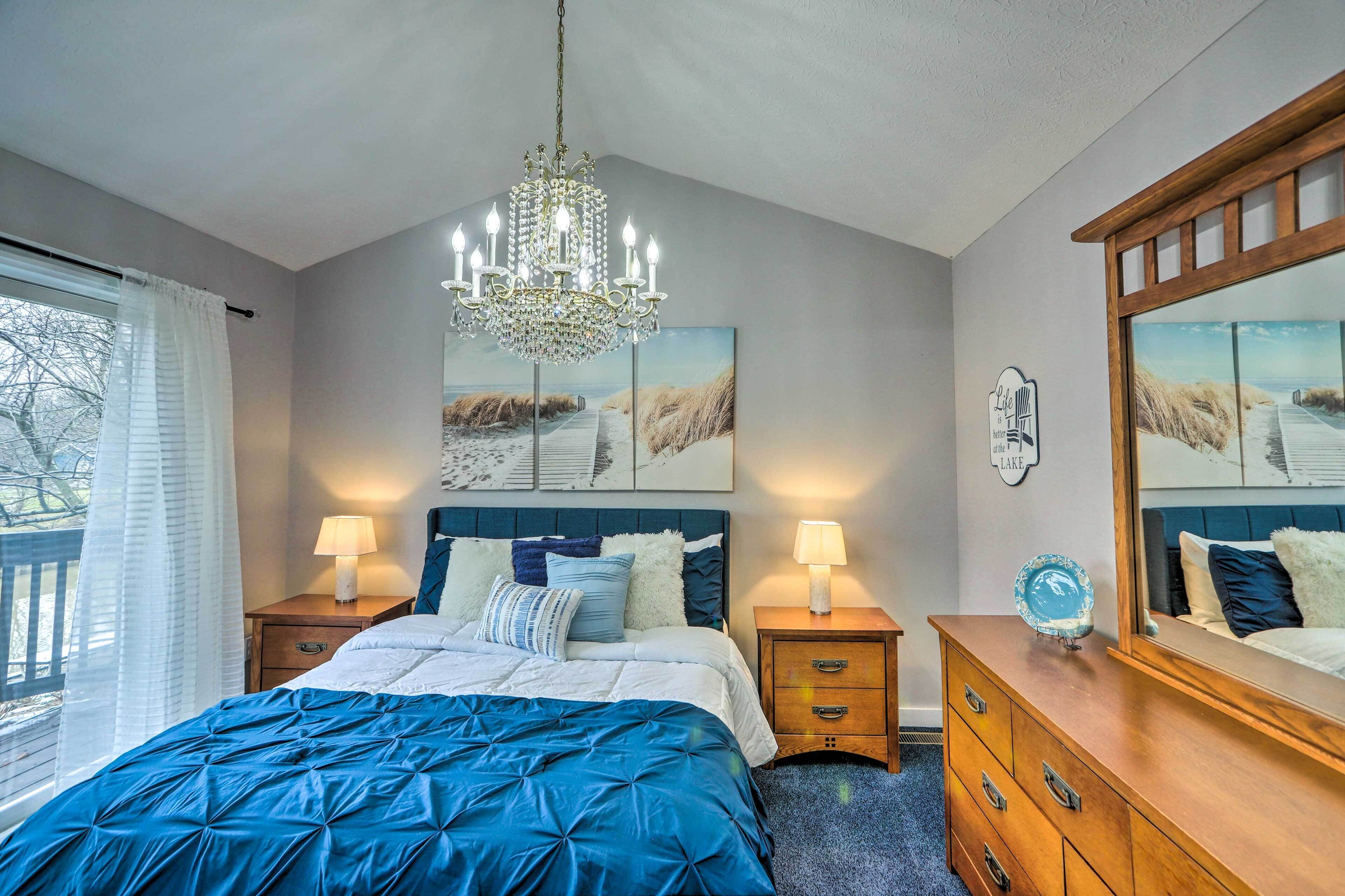 Quarto com cama grande, duas mesas de cabeceira, cômoda, lustre e obras de arte nas paredes.