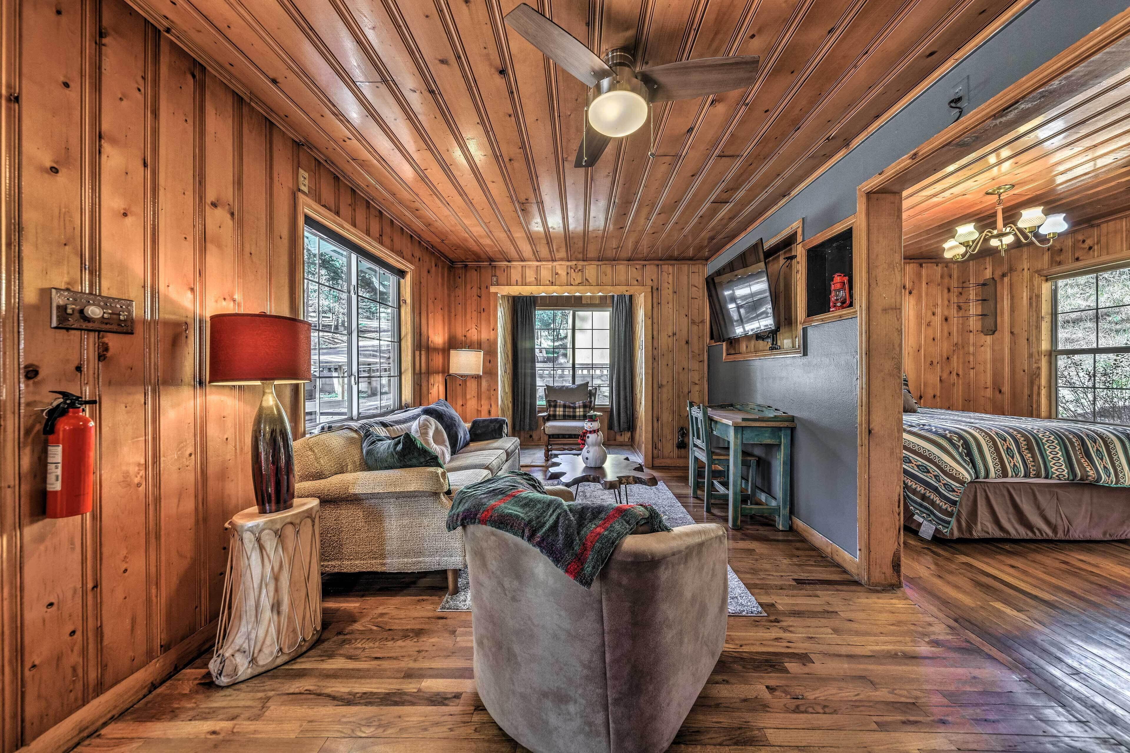 A cozy cabin interior with wooden walls, a ceiling fan, a sofa, a bed, and a small table.