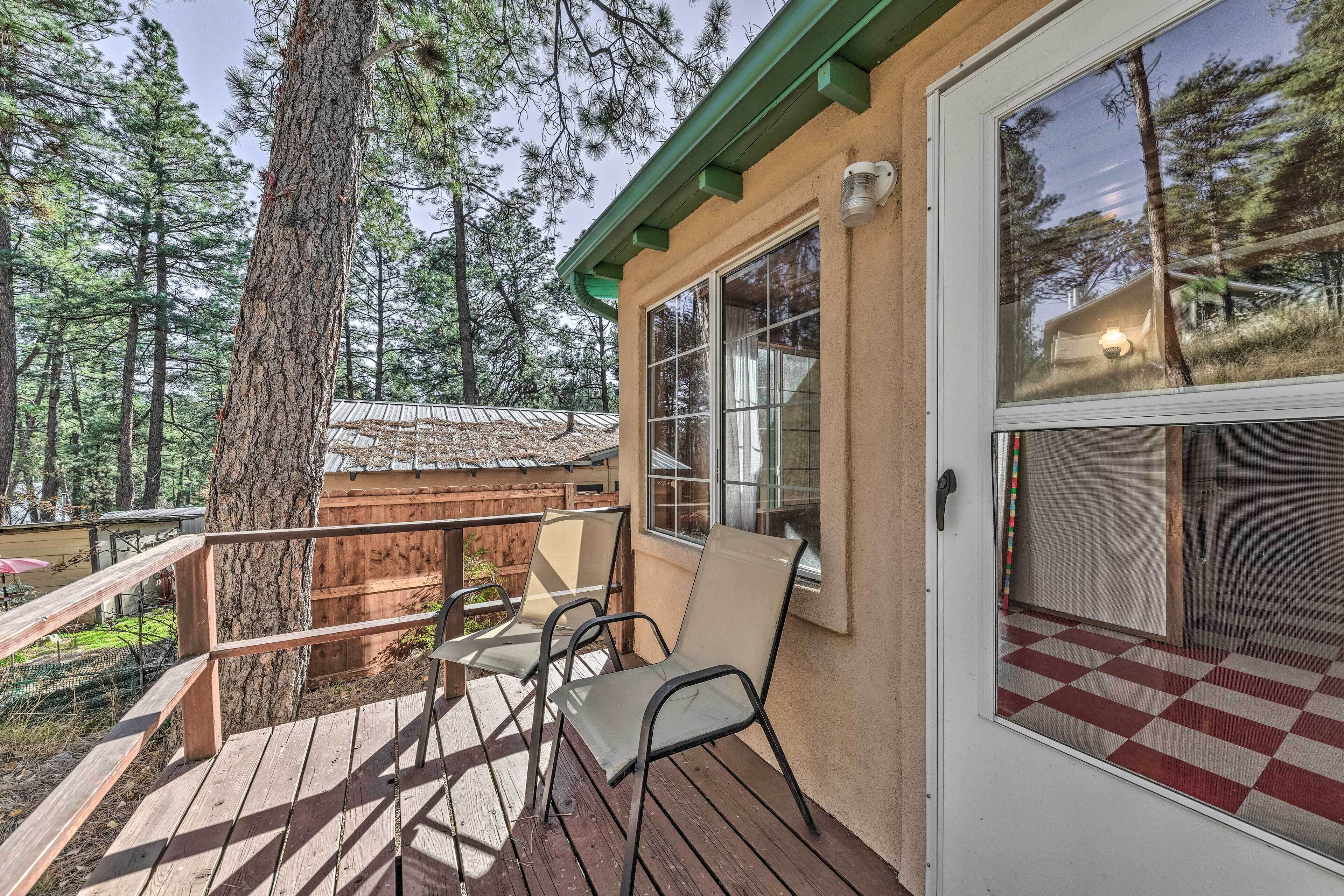 Une terrasse en bois avec des chaises, une vue sur une forêt et un bâtiment dont le sol est à carreaux.