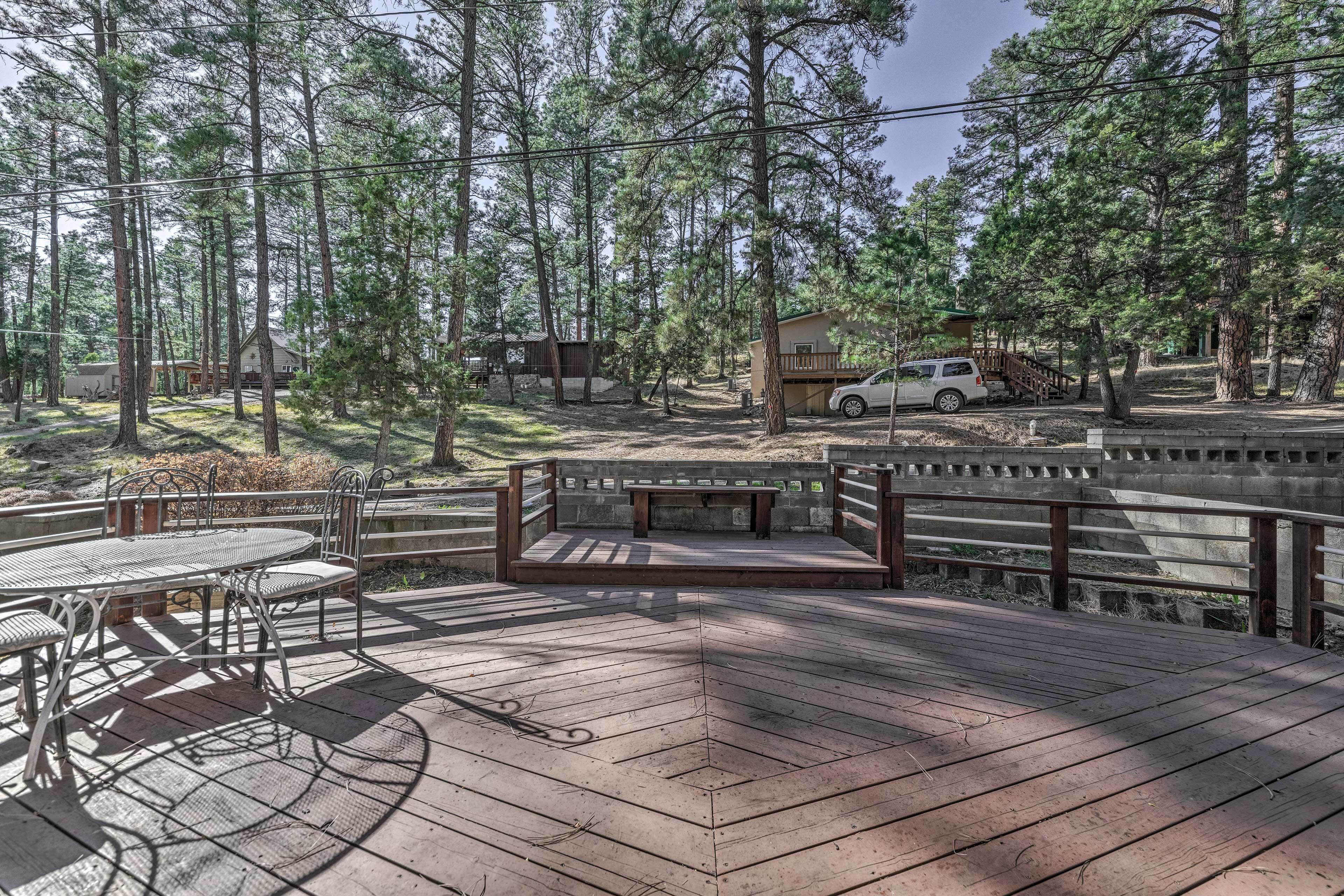 Une terrasse en bois avec une table et des chaises en métal, entourée de grands pins.