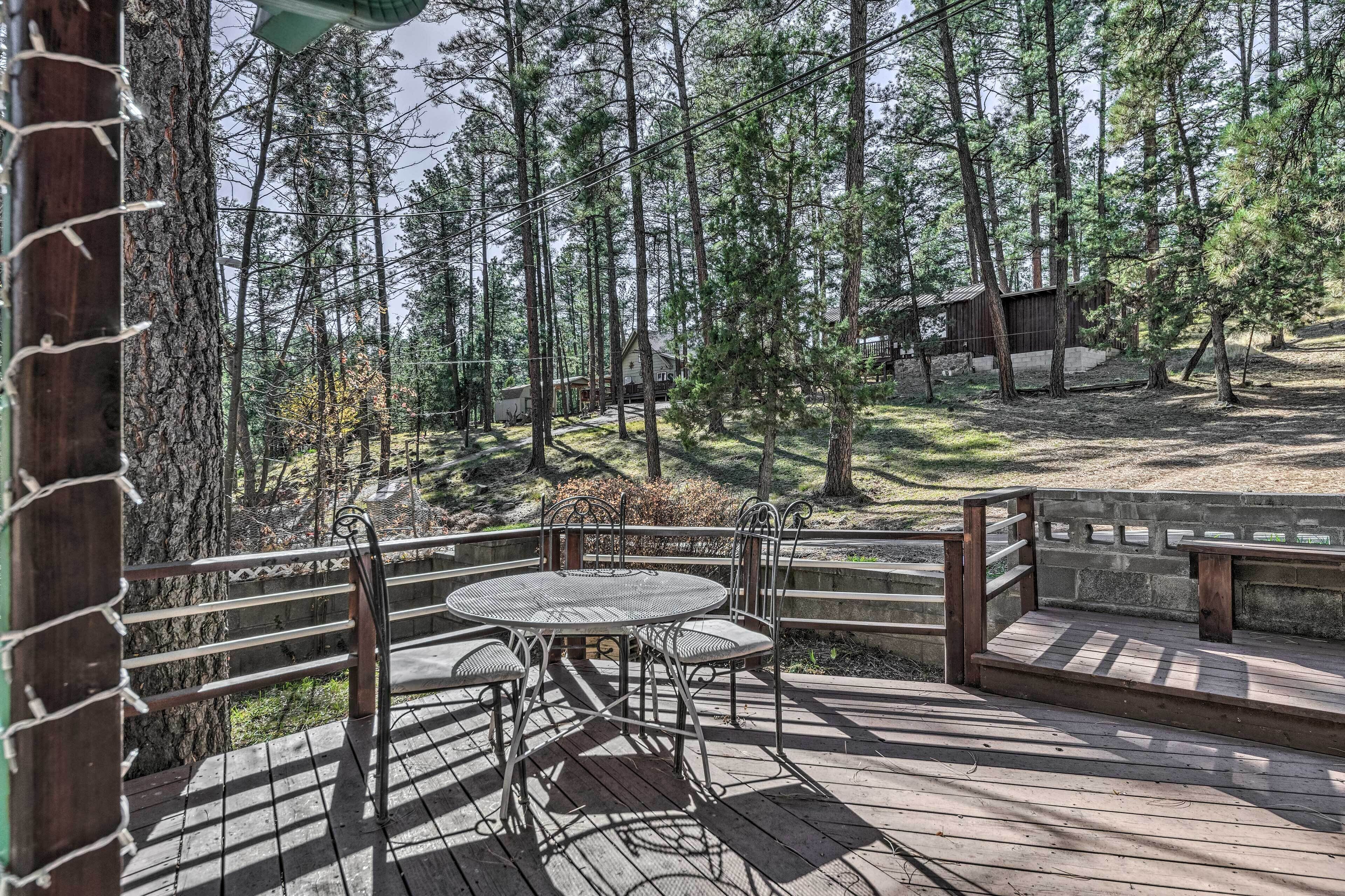 A wooden deck with a metal table and chairs, surrounded by a wooden fence and trees.
