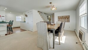 A spacious dining area with a wooden table and chairs, a staircase leading to another room, and a large window providing natural light. - Lakefront Michigan Cottage - Deck, Grill & Kayaks! (Sturgis)