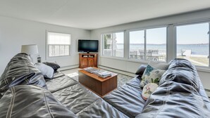 A living room with a large window, a flat-screen TV, and a wooden coffee table. - Lakefront Michigan Cottage - Deck, Grill & Kayaks! (Sturgis)