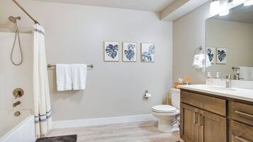 A bathroom with a bathtub, toilet, and vanity with a mirror. There are three framed pictures on the wall and a towel rack with towels.