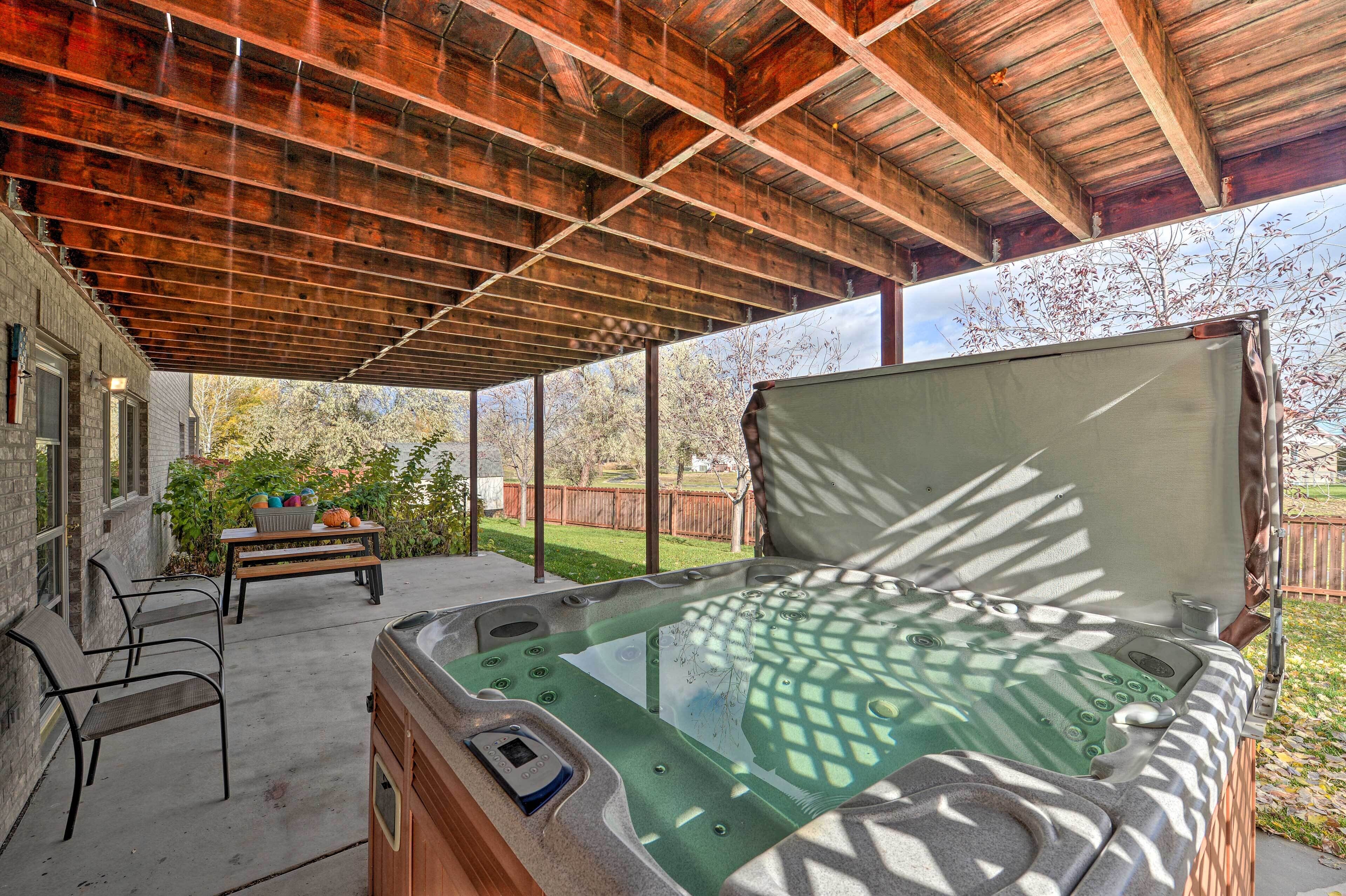 A hot tub under a wooden roof with a table and chairs nearby.