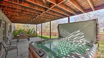 A hot tub under a wooden roof with a table and chairs nearby.