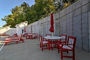 Ein Außenbereich mit einer Terrasse, ausgestattet mit roten und weißen Streifenliegen sowie Tischen, umgeben von einer Betonmauer und Bäumen.