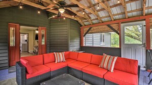 A covered outdoor seating area with a red sectional sofa and a small table, wooden beams, and a ceiling fan. - Altmar Family Home w/ Rivers & Trails Nearby! (Altmar)