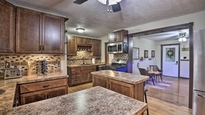 Una cocina con encimeras de granito, armarios de madera y un microondas integrado. Hay un comedor con mesa y sillas.