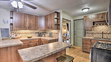 A kitchen with wooden cabinets, granite countertops, a gas stove, and a ceiling fan.