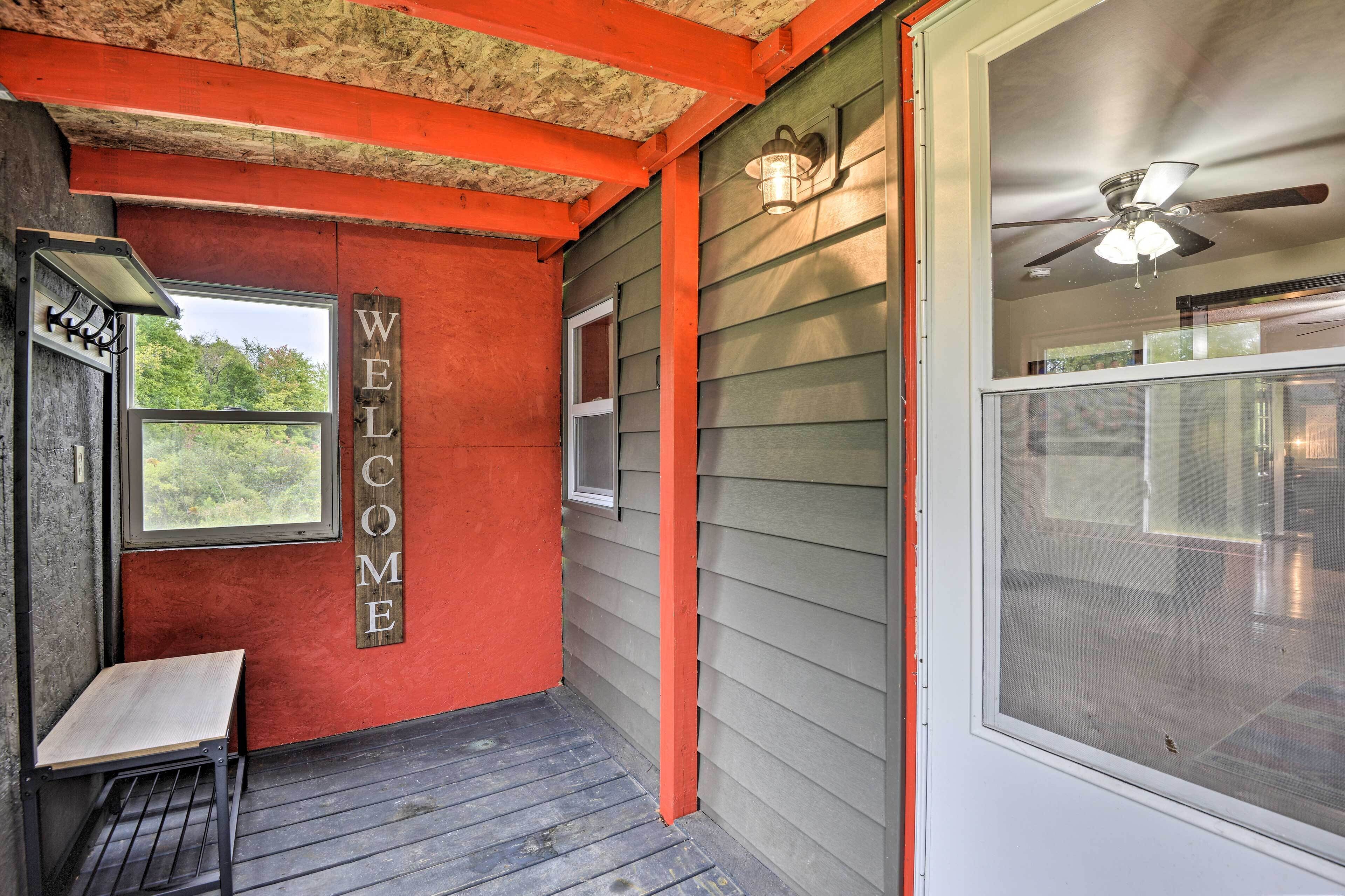 A room with a 'WELCOME' sign, a ceiling fan, a window, and a bench.
