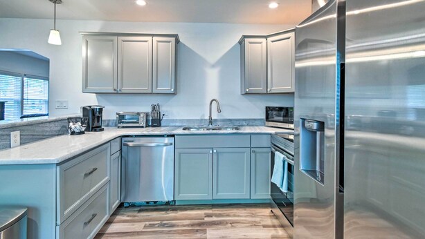 A modern kitchen with light blue cabinets, stainless steel appliances, and a wooden floor.