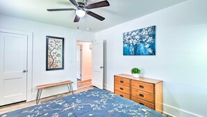 A bedroom with a bed, a wooden dresser, a ceiling fan, and a painting on the wall.