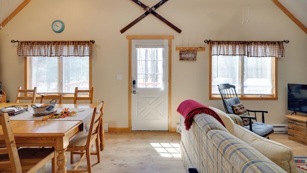A cozy living room with a wooden ceiling, a sofa, a television, and a dining area with a table and chairs. - Walk to Beach: Pocono Lake Cabin w/ Pool Access! (Pocono Lake)