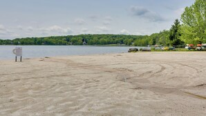 A sandy beach with a sign, a lake, and a forested hill in the background. - Walk to Beach: Pocono Lake Cabin w/ Pool Access! (Pocono Lake)