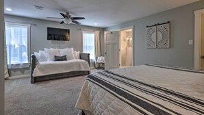 A bedroom with a large bed, a smaller bed, a ceiling fan, a TV, and a door leading to another room. - Cozy Retreat w/ Hot Tub & Fire Pit: Close to Main! (Fredericksburg)