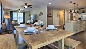 A dining area with a wooden table set for four, a ceiling fan, and a kitchen area with a refrigerator and cabinets. - Cozy Retreat w/ Hot Tub & Fire Pit: Close to Main! (Fredericksburg)