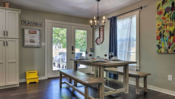 A dining area with a wooden table and benches, a chandelier, and a view of the outdoors. - Cozy Retreat w/ Hot Tub & Fire Pit: Close to Main! (Fredericksburg)