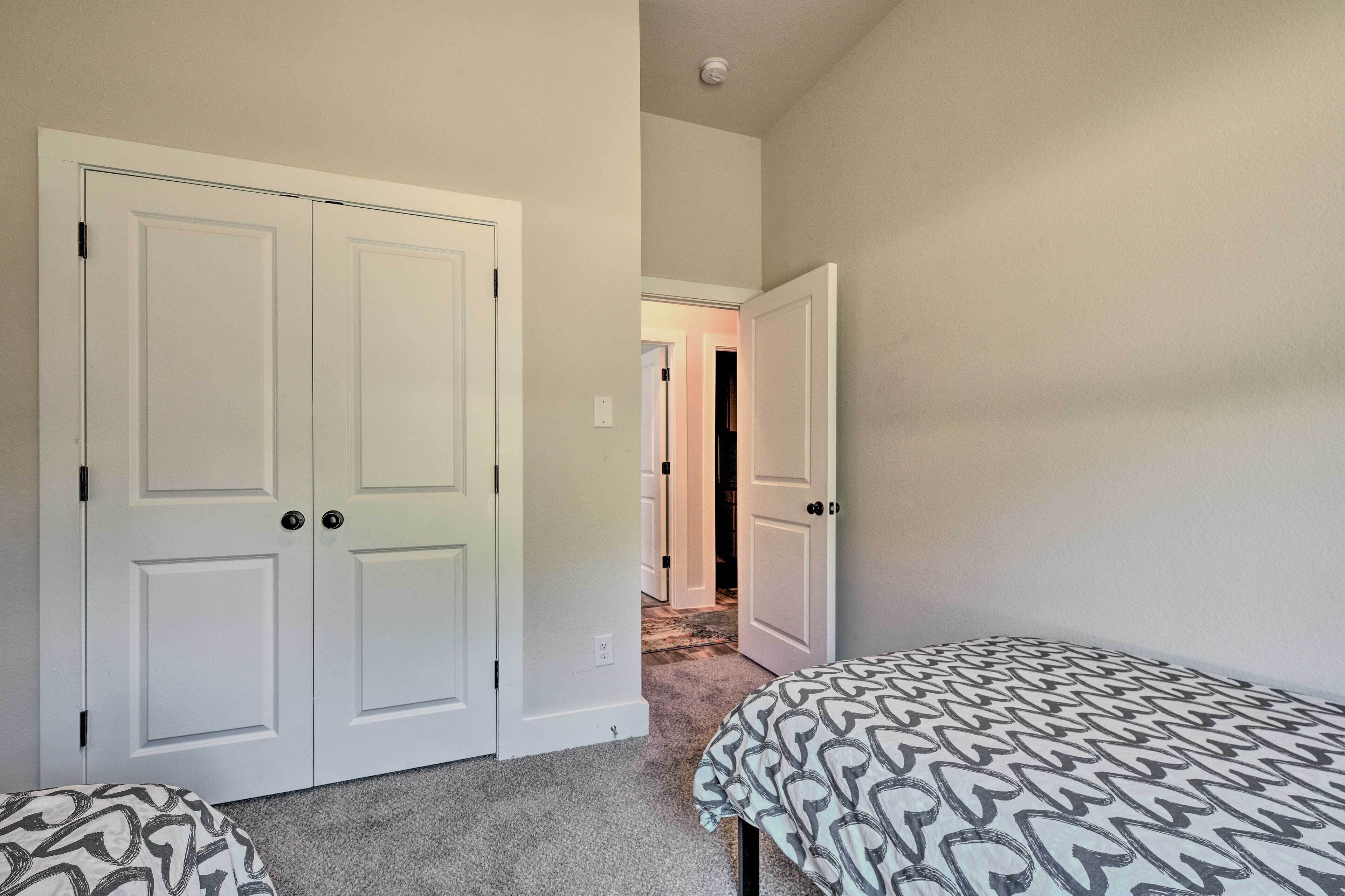 Quarto com duas camas de solteiro, uma porta branca e piso coberto por carpete.