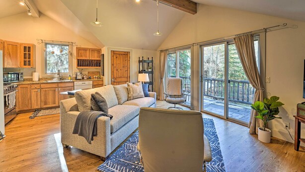A spacious living area with a large sofa, a chair, and a dining table. There is a kitchen with wooden cabinets and a large window. - Ketchum Couple's Retreat: 1 Mi to Sun Valley! (Ketchum)
